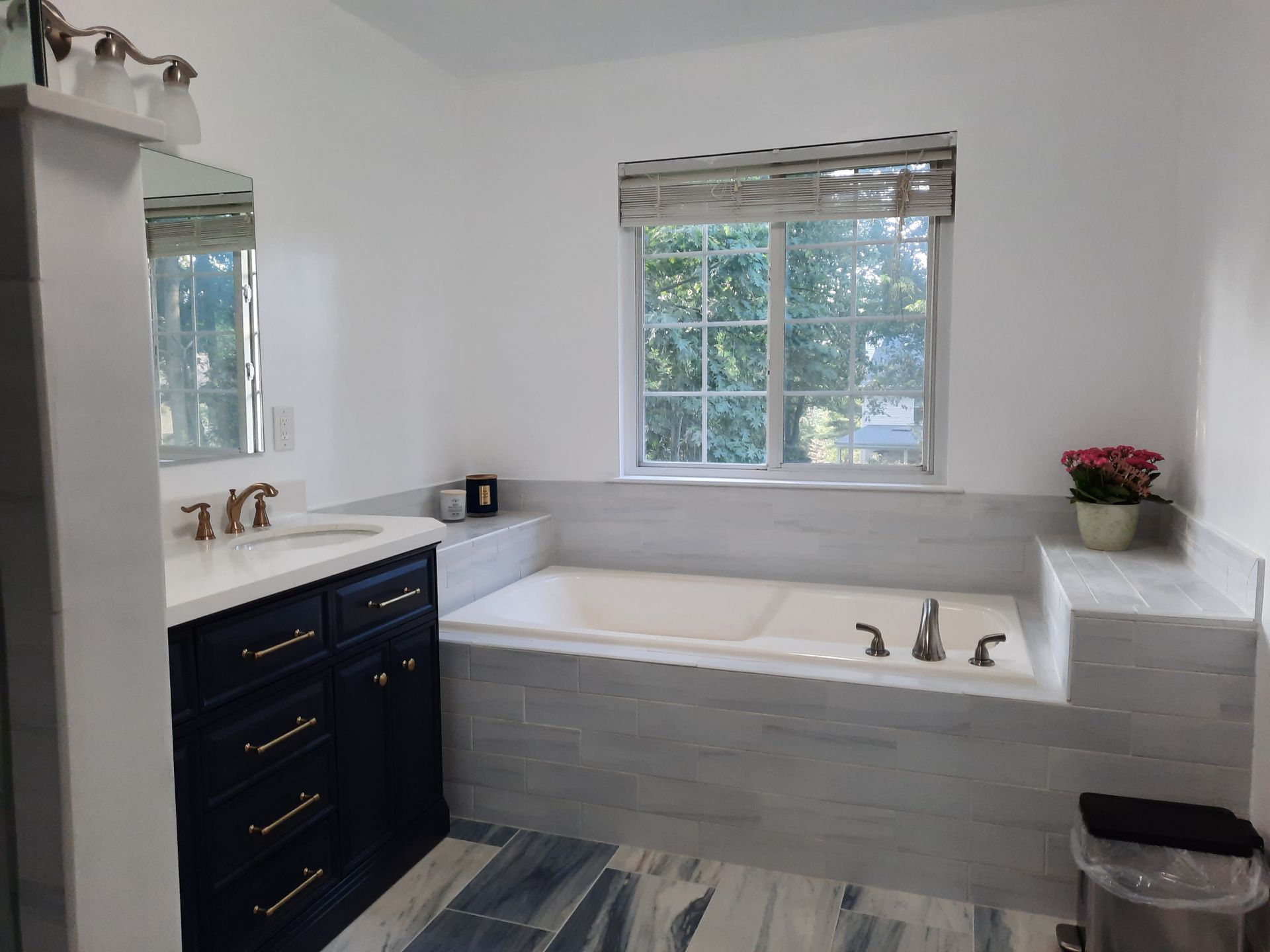 A bathroom with a tub , sink , mirror and window.