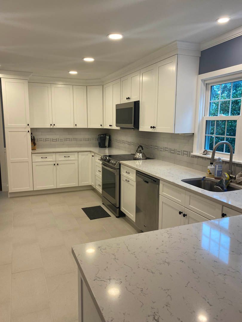 A kitchen with white cabinets , stainless steel appliances , a sink , and a window.