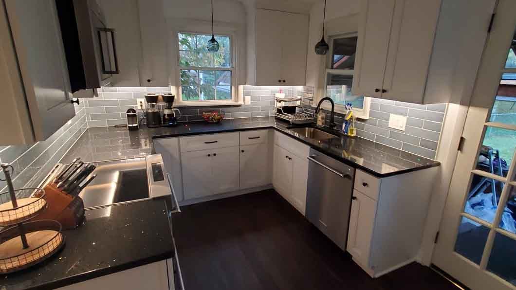 A kitchen with white cabinets , black counter tops , stainless steel appliances and a window.