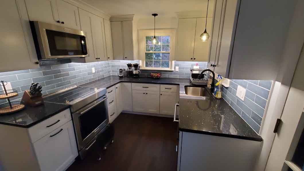 A kitchen with white cabinets , black counter tops , stainless steel appliances and a window.
