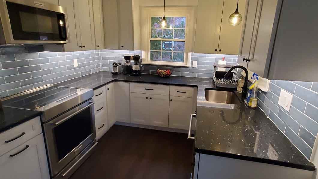 A kitchen with white cabinets , black counter tops , stainless steel appliances and a sink.