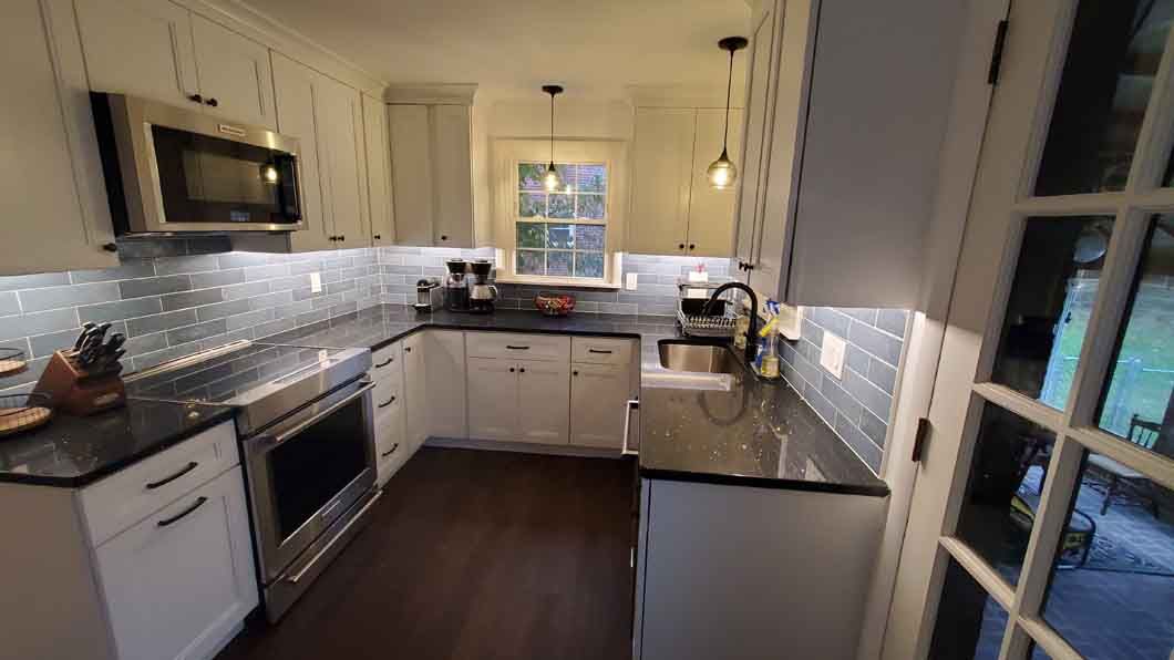 A kitchen with white cabinets , black counter tops , stainless steel appliances and a window.