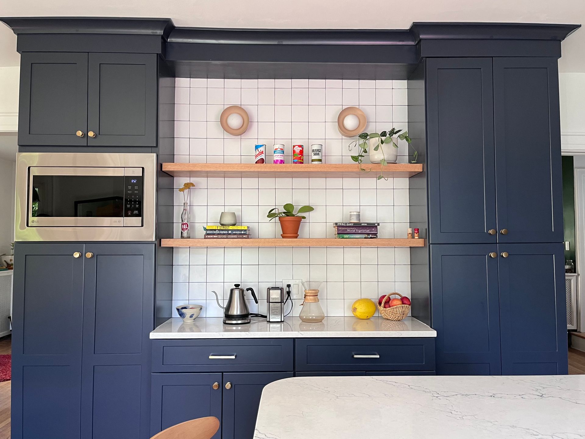 A kitchen with blue cabinets , white counter tops , and a microwave.