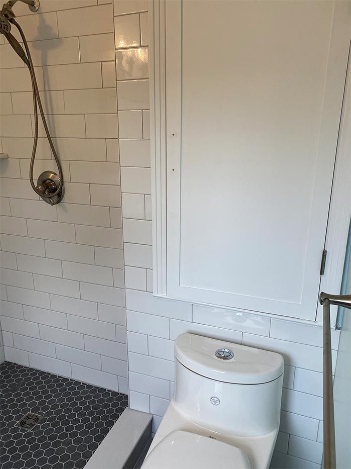 A bathroom with a toilet , shower , and cabinet.