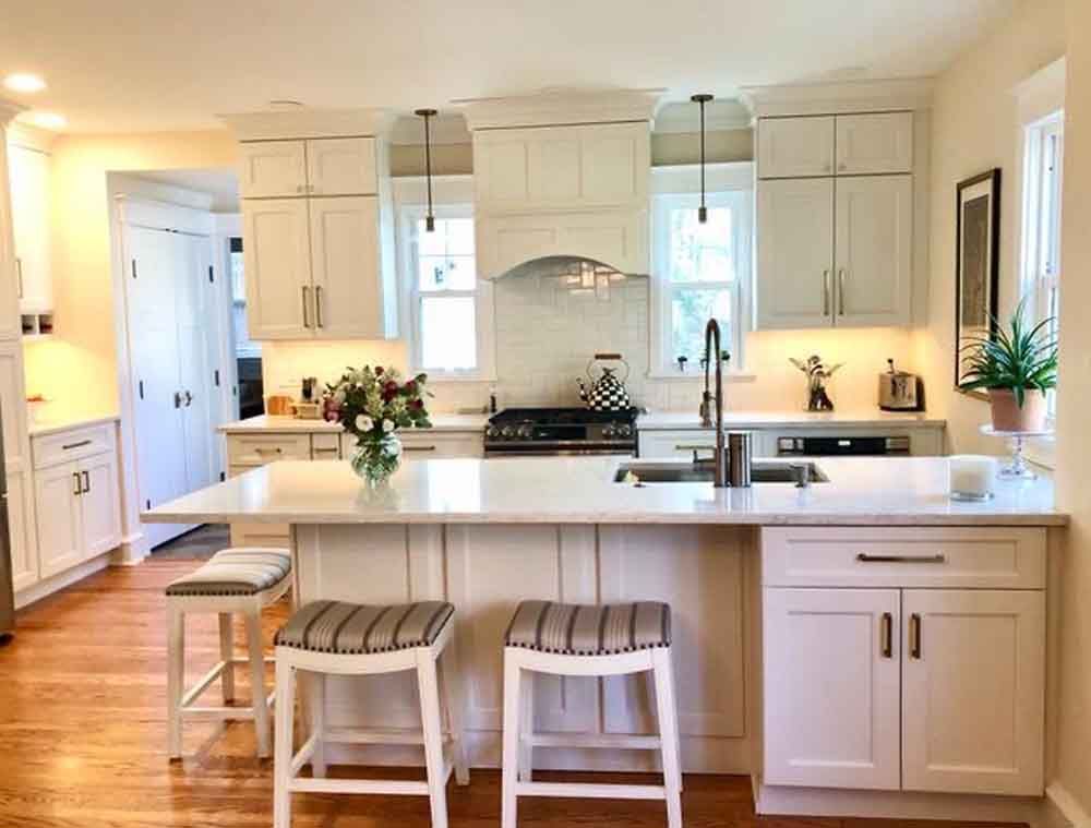 A kitchen with white cabinets and stools and a large island.