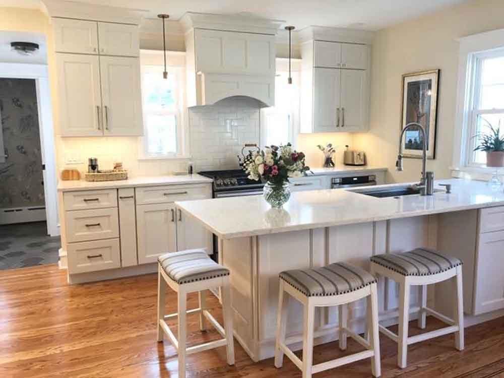 A kitchen with white cabinets and stools and a large island in the middle.