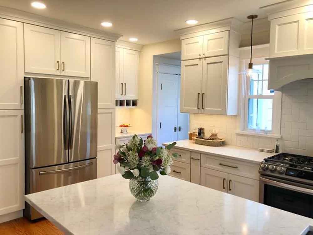 A kitchen with white cabinets and stainless steel appliances and a vase of flowers on the counter.