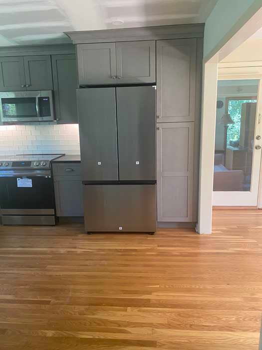 A kitchen with gray cabinets , a stainless steel refrigerator , a stove , and a microwave.