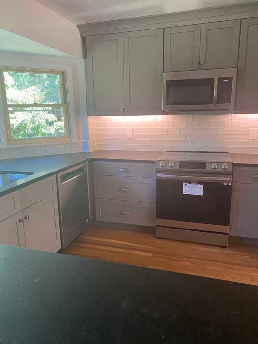 A kitchen with gray cabinets , stainless steel appliances , a black counter top , and a window.