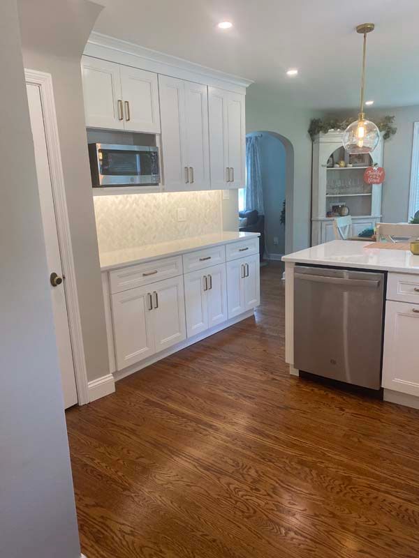 A kitchen with white cabinets and hardwood floors and a stainless steel dishwasher.