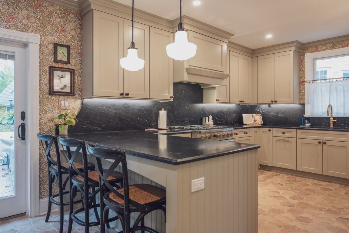 A kitchen with a large island and stools and a clock on the wall.