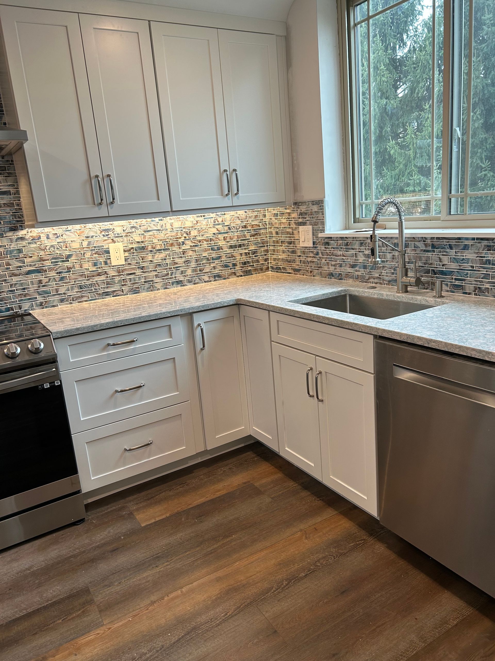 A kitchen with white cabinets , stainless steel appliances , a sink , and a window.