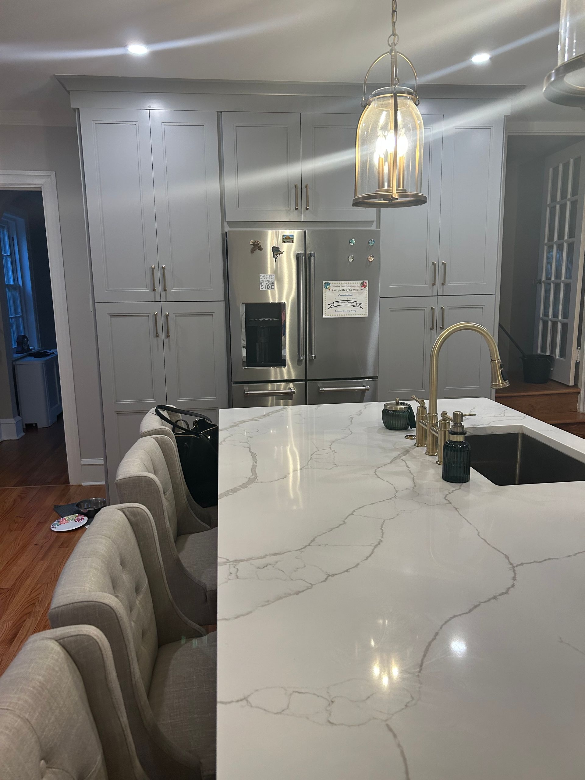 A kitchen with white cabinets , stainless steel appliances , a sink and a refrigerator.