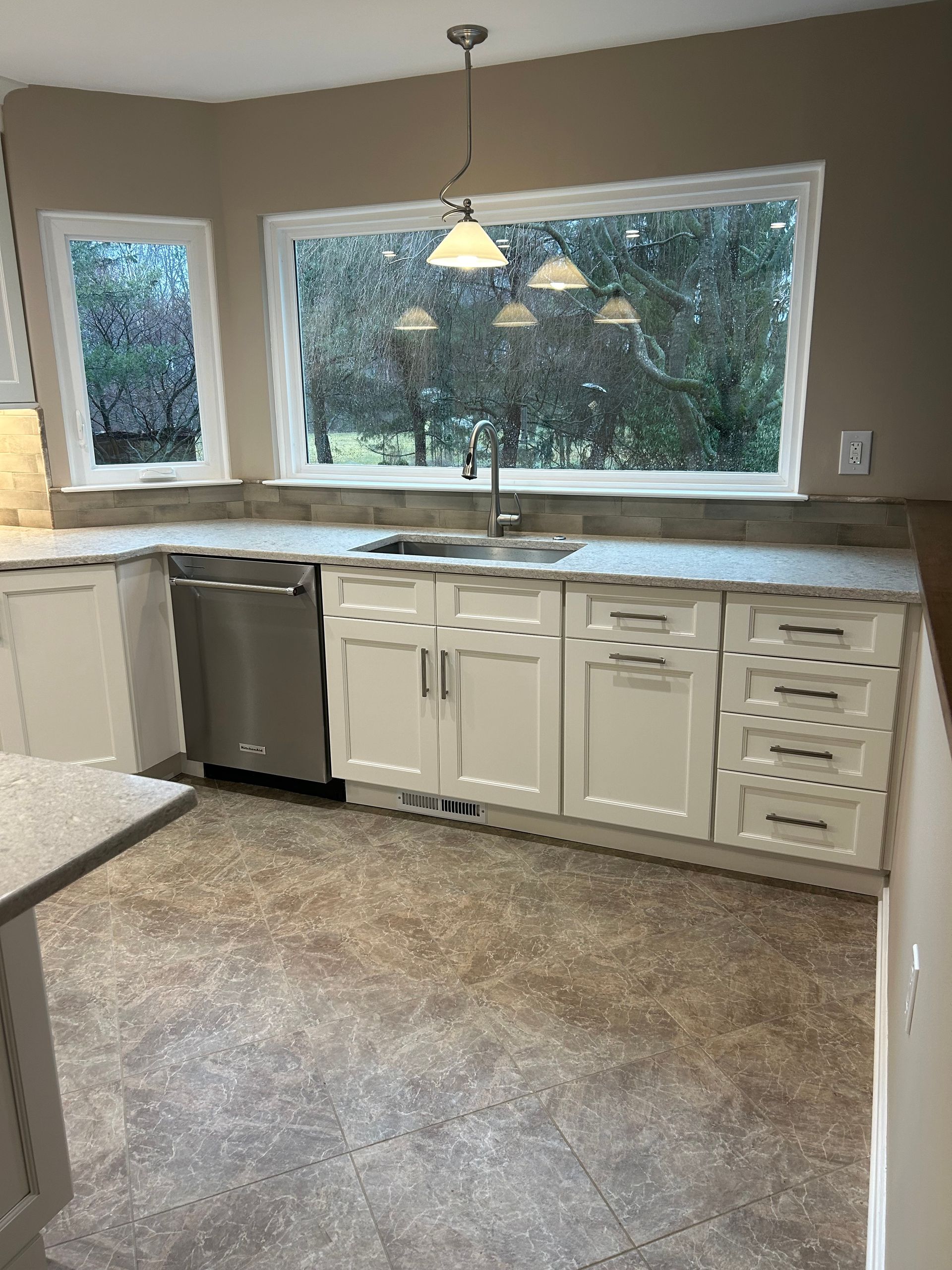 A kitchen with white cabinets , a sink , a dishwasher , and a large window.