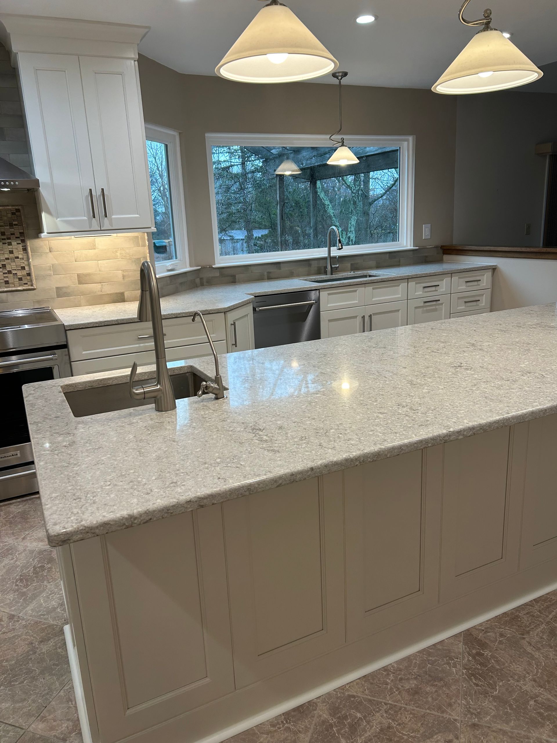 A kitchen with white cabinets , granite counter tops , stainless steel appliances and a large island.