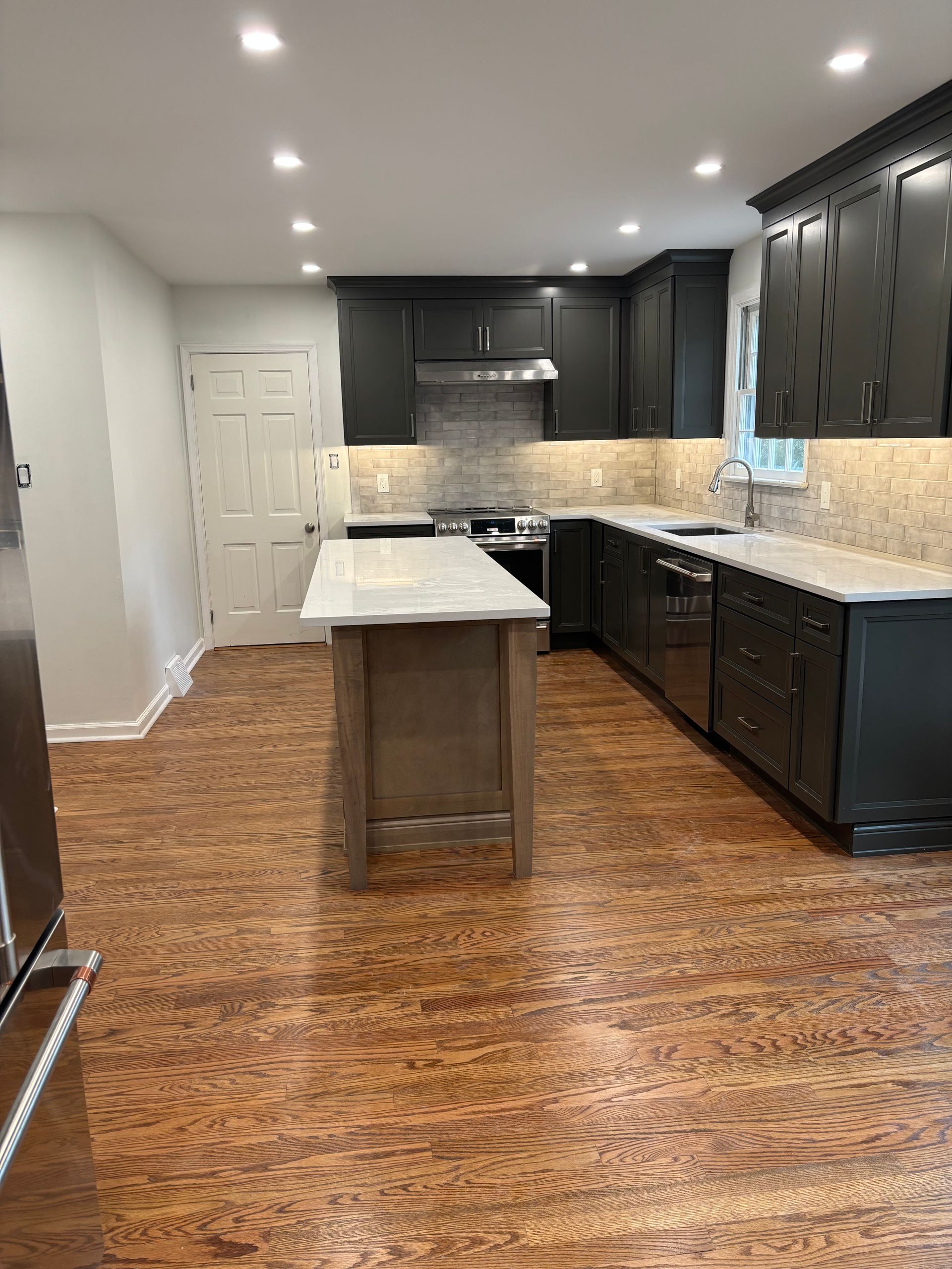 A kitchen with black cabinets and stainless steel appliances and a large island.
