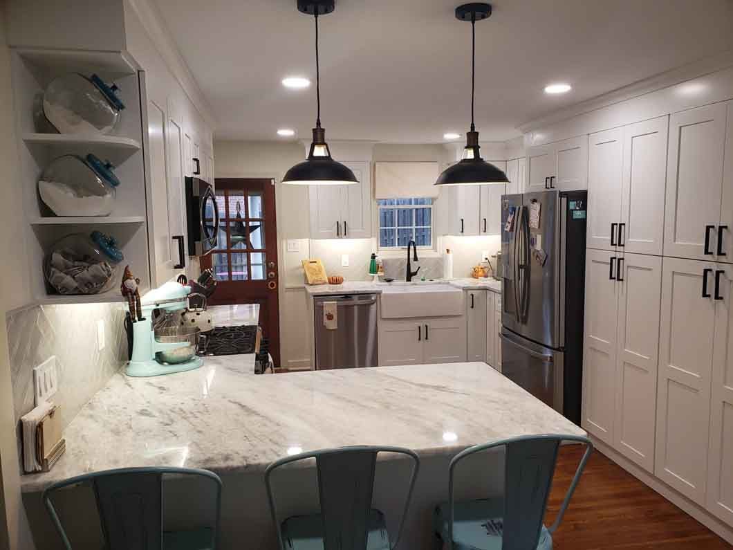 A kitchen with white cabinets , marble counter tops , stainless steel appliances and a large island.