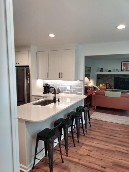 A kitchen with a large island and stools and a living room in the background.