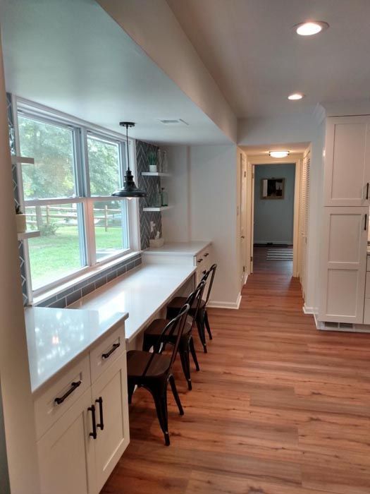 A kitchen with hardwood floors , white cabinets , a desk and chairs.