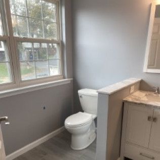 A bathroom with a toilet , sink , mirror and window.