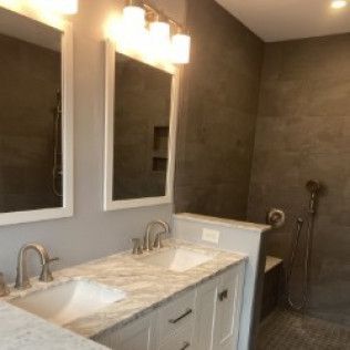 A bathroom with two sinks , two mirrors , and a walk in shower.