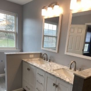 A bathroom with two sinks , two mirrors and a window.