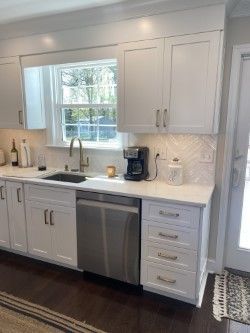 A kitchen with white cabinets , stainless steel appliances , a sink , and a window.