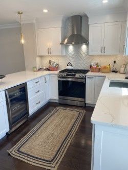 A kitchen with white cabinets , stainless steel appliances , and a rug on the floor.