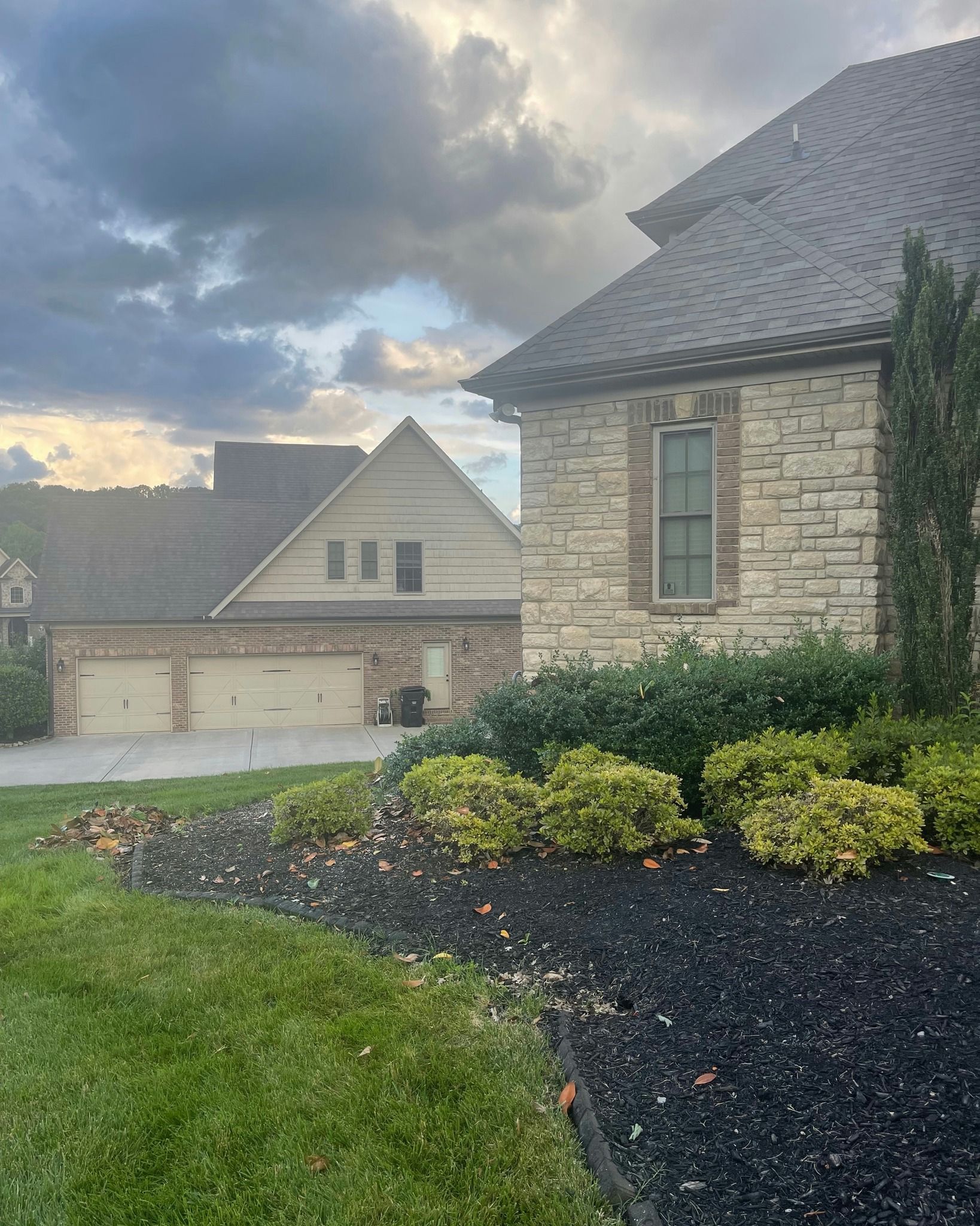 Stone house exterior with landscaping and another building behind it under a cloudy sky.