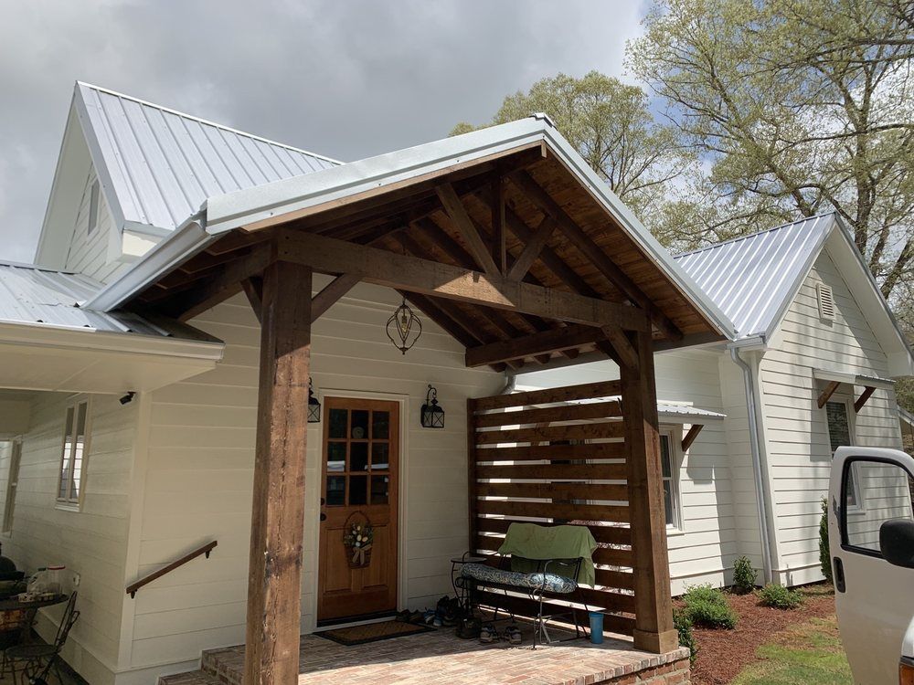 A white house with a wooden porch and a metal roof.