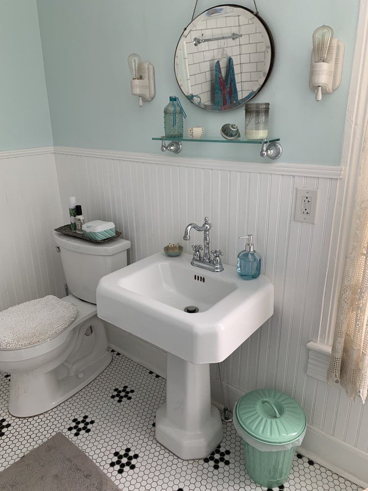 A bathroom with a toilet , sink , mirror and trash can.
