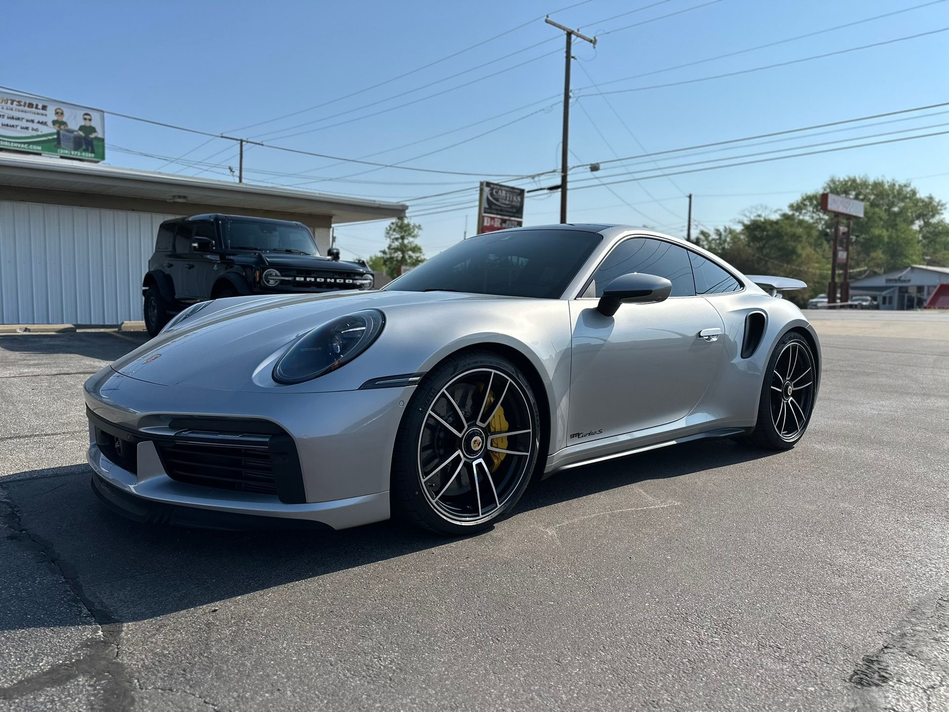 Silver Porsche sports car parked outside on a sunny day. Black wheels, yellow calipers.