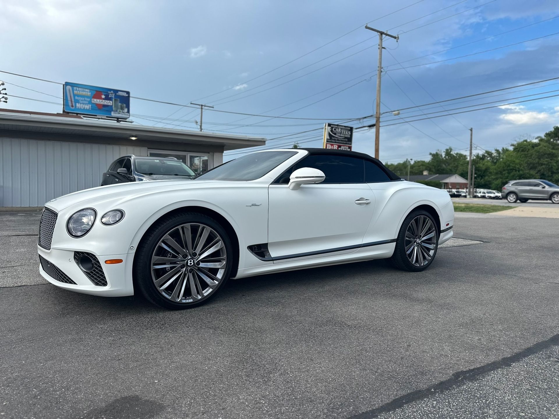 White Bentley convertible parked on asphalt in front of a building.