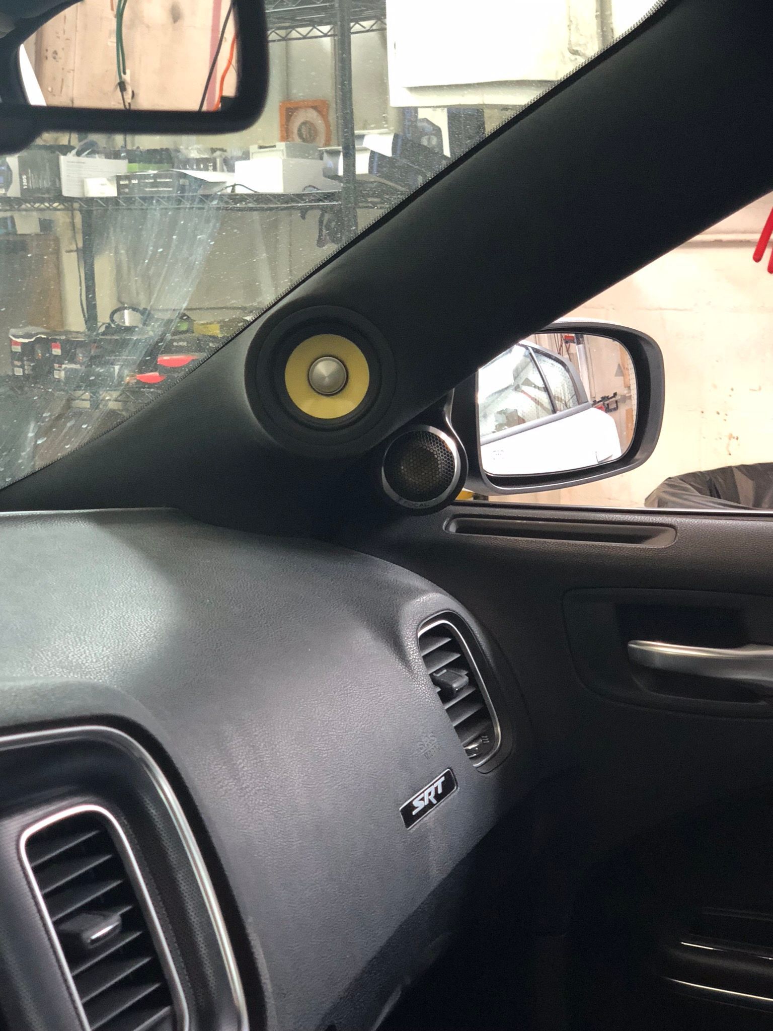 Car interior with speaker mounted on pillar, dashboard, side mirror visible.