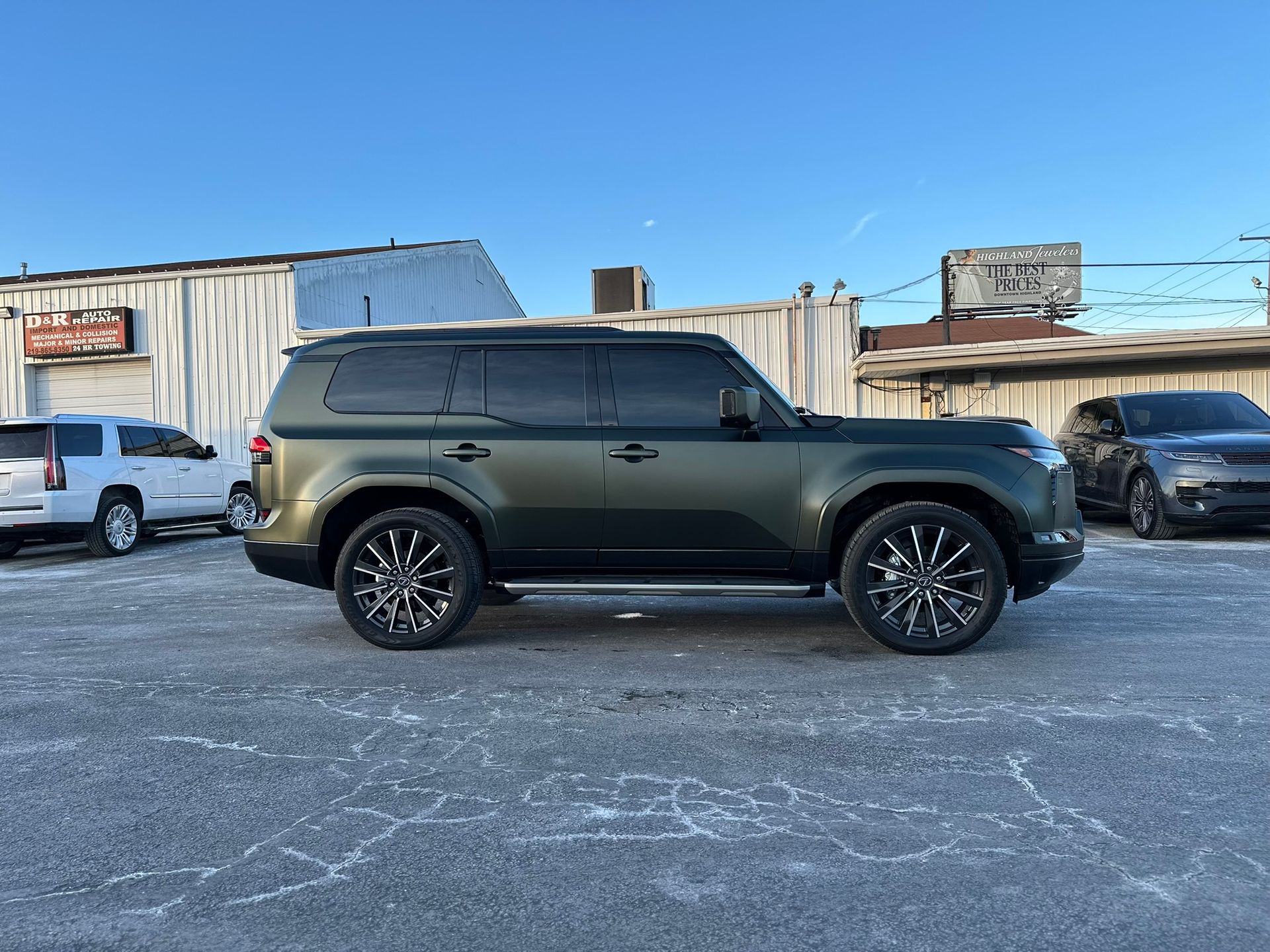 Green Land Rover Defender parked on a cracked lot with black and silver rims.