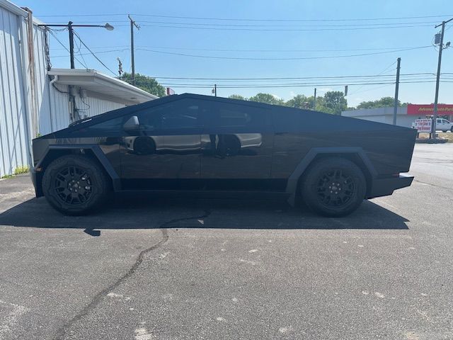 Black Tesla Cybertruck parked on asphalt near a building, with tinted windows and dark wheels.