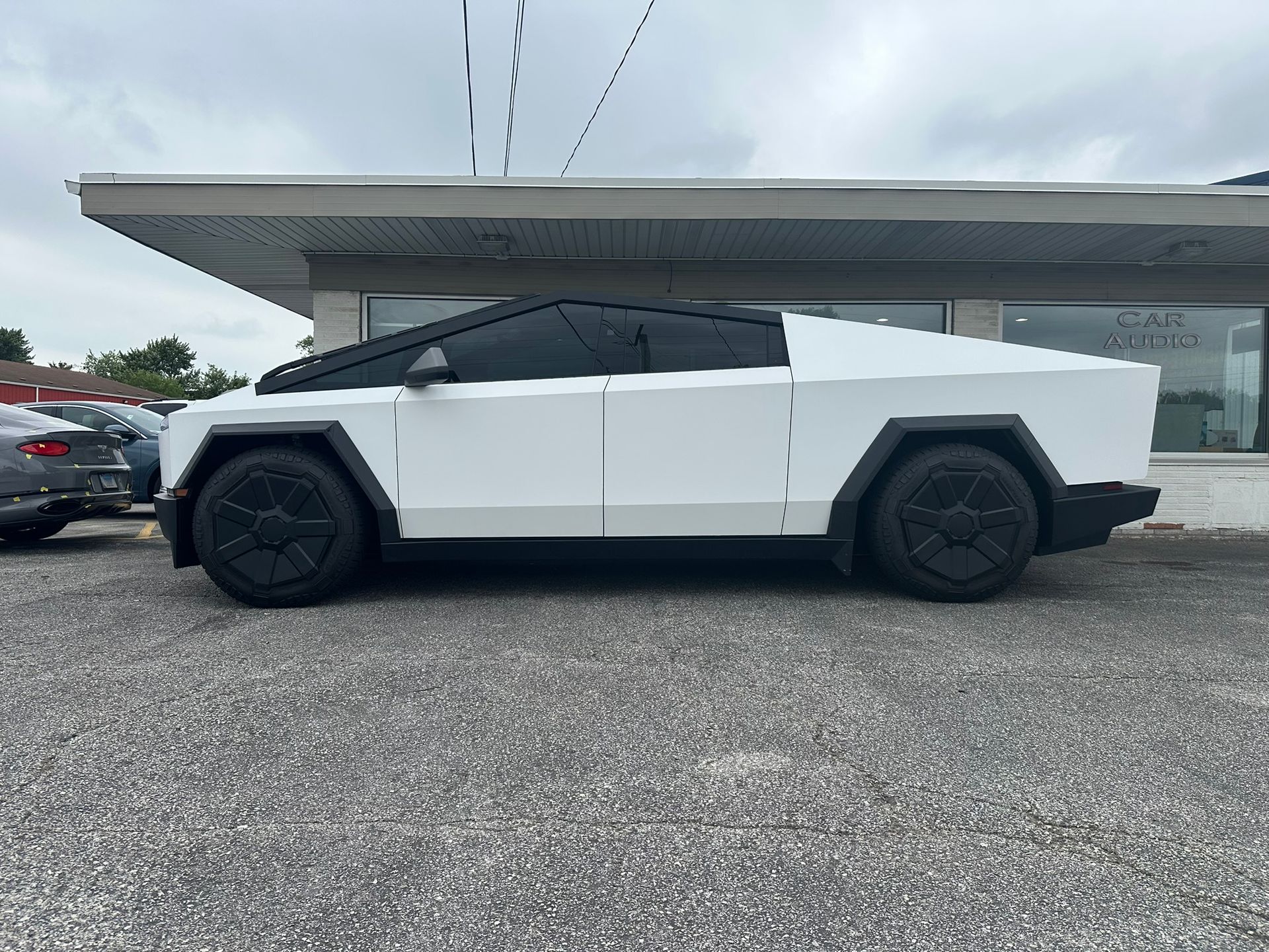 White Tesla Cybertruck parked on gravel. Black tires, tinted windows. Cloudy day.