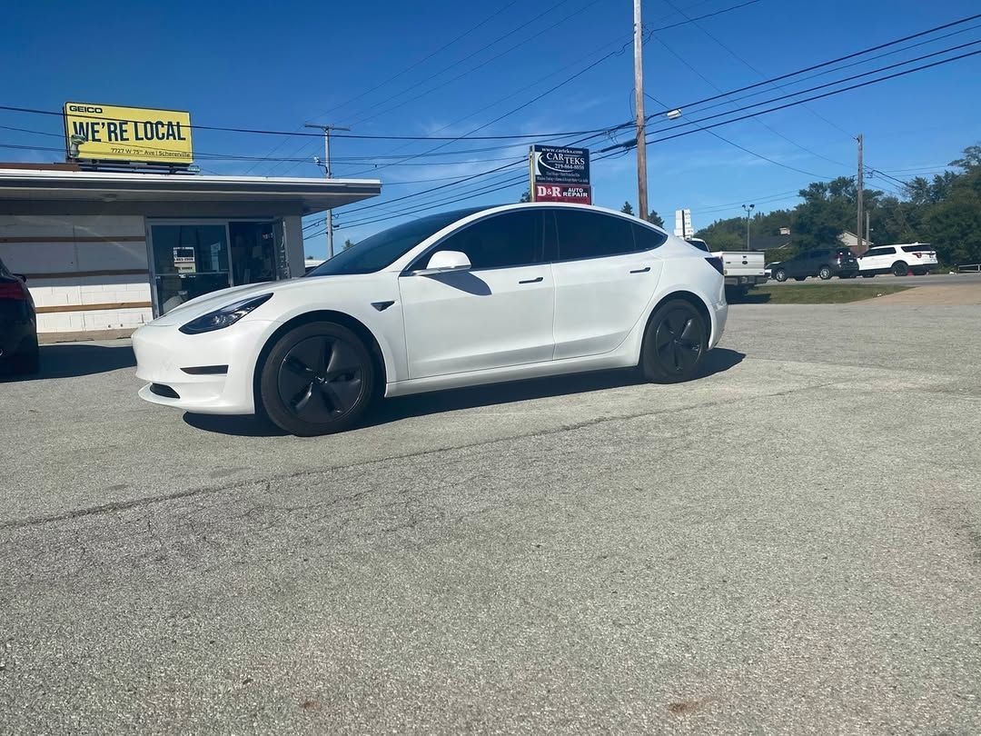 White Tesla parked on gravel in front of a building with a business sign.