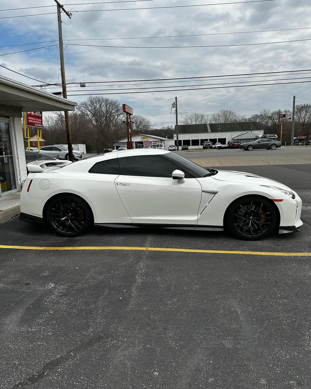 White Nissan GT-R parked on asphalt next to a storefront under a cloudy sky.