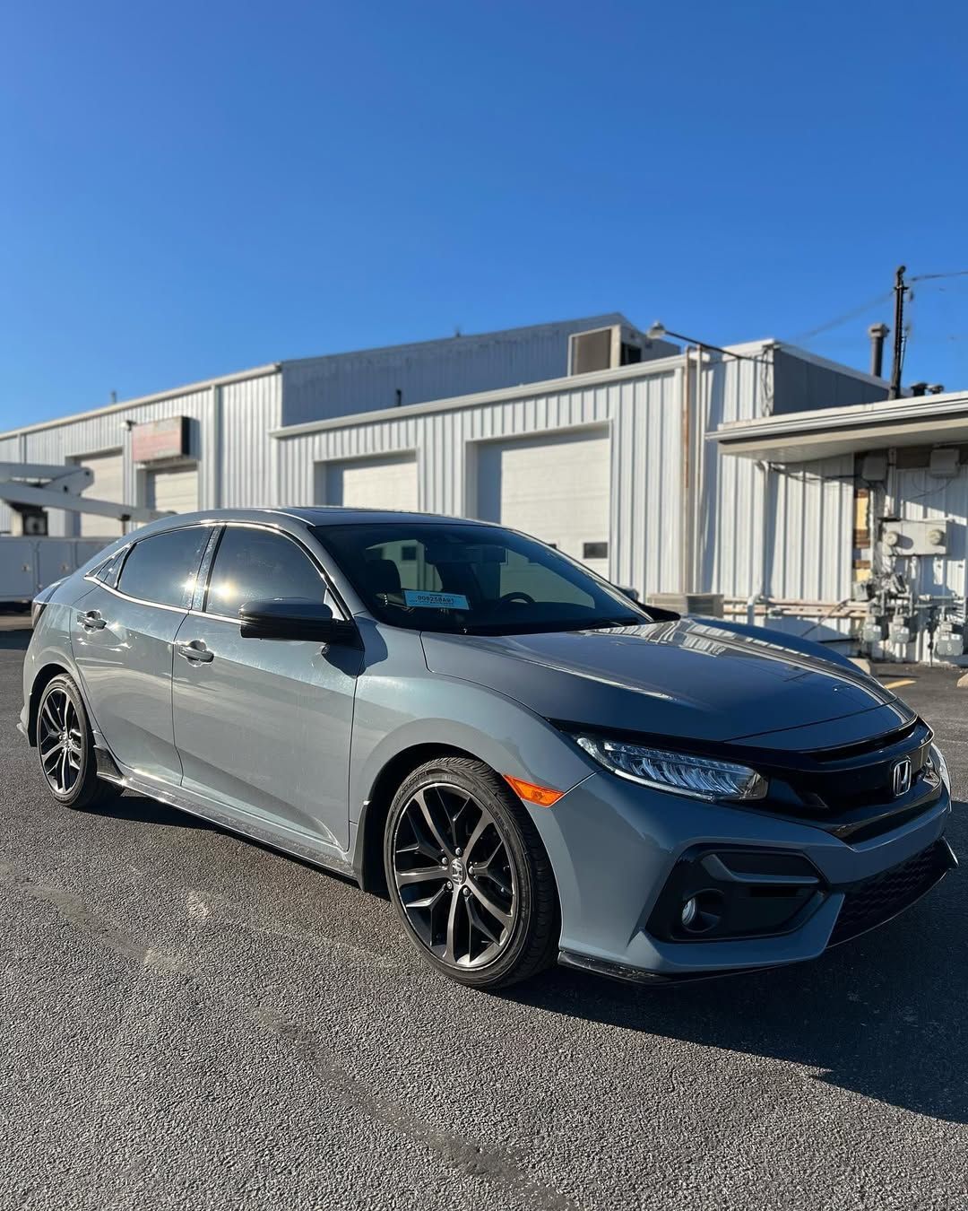 Gray Honda Civic hatchback parked on gravel in front of a white building on a sunny day.