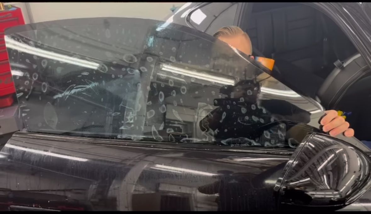 Person applying tint to a car window in a garage.