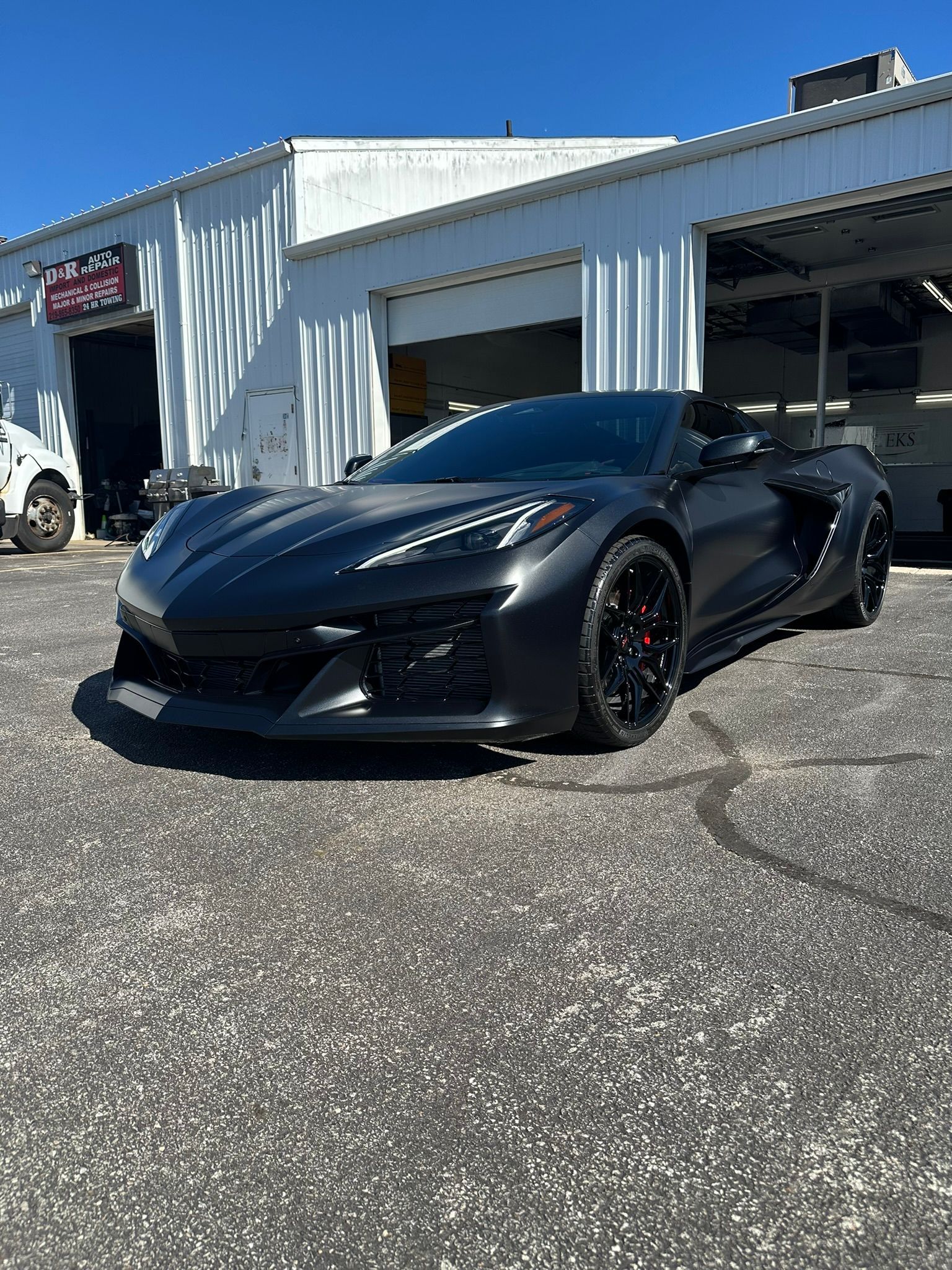Black Corvette convertible parked in front of a white garage on a sunny day.