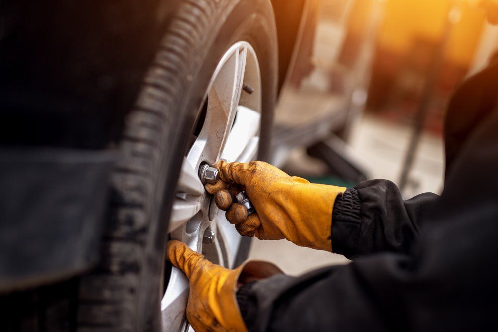 Person In Yellow Gloves Using A Wrench To Tighten Lug Nuts On A Car Tire
