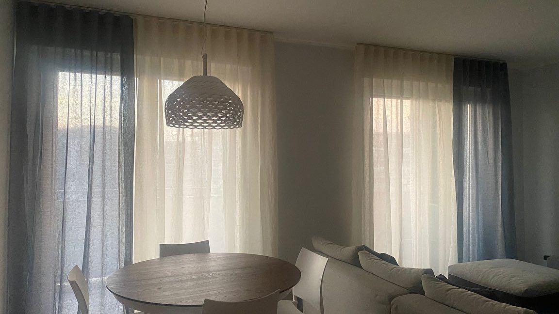 Un soggiorno con tavolo, divano, sedie e tende.