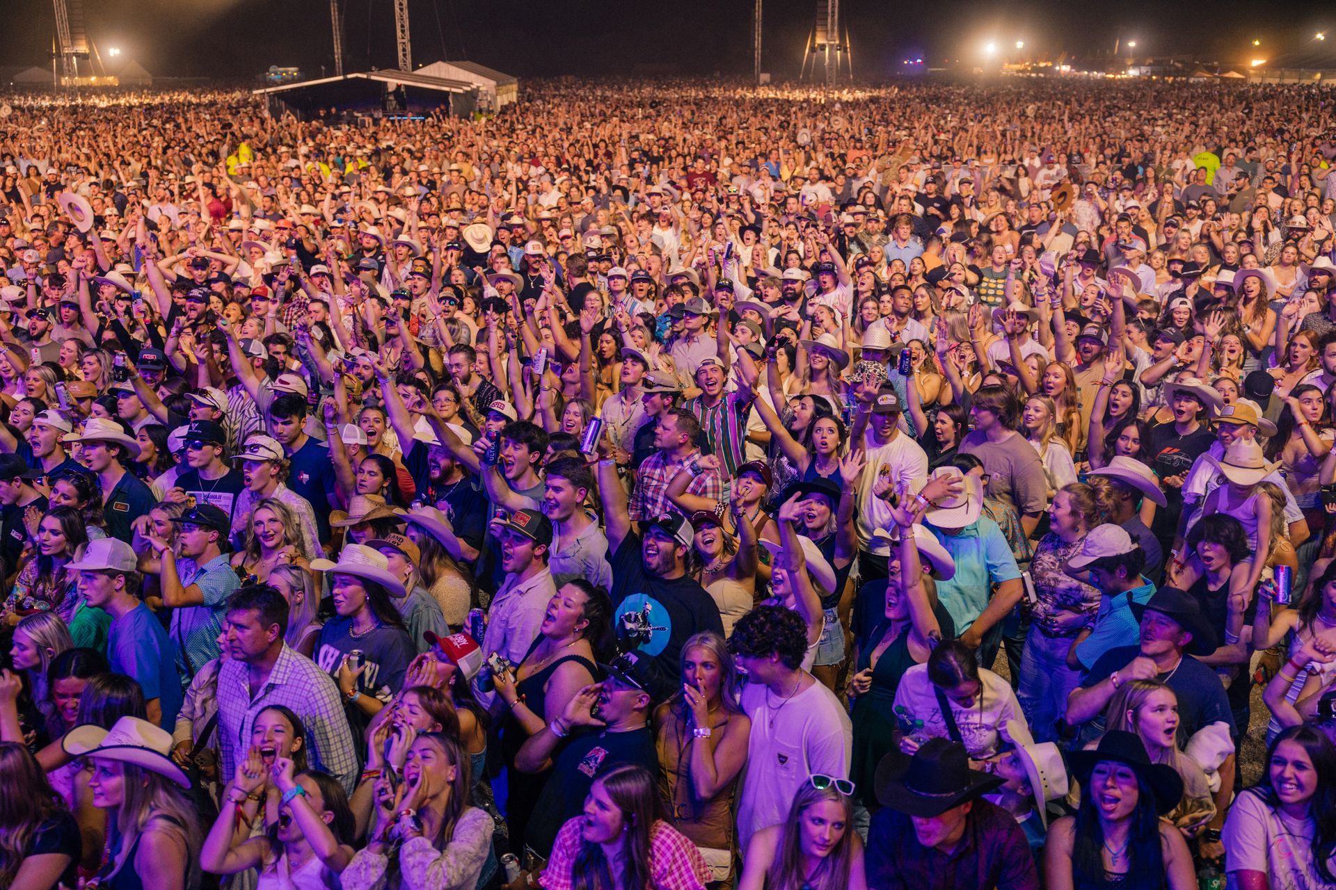 A large crowd of people are standing in a field at a concert.