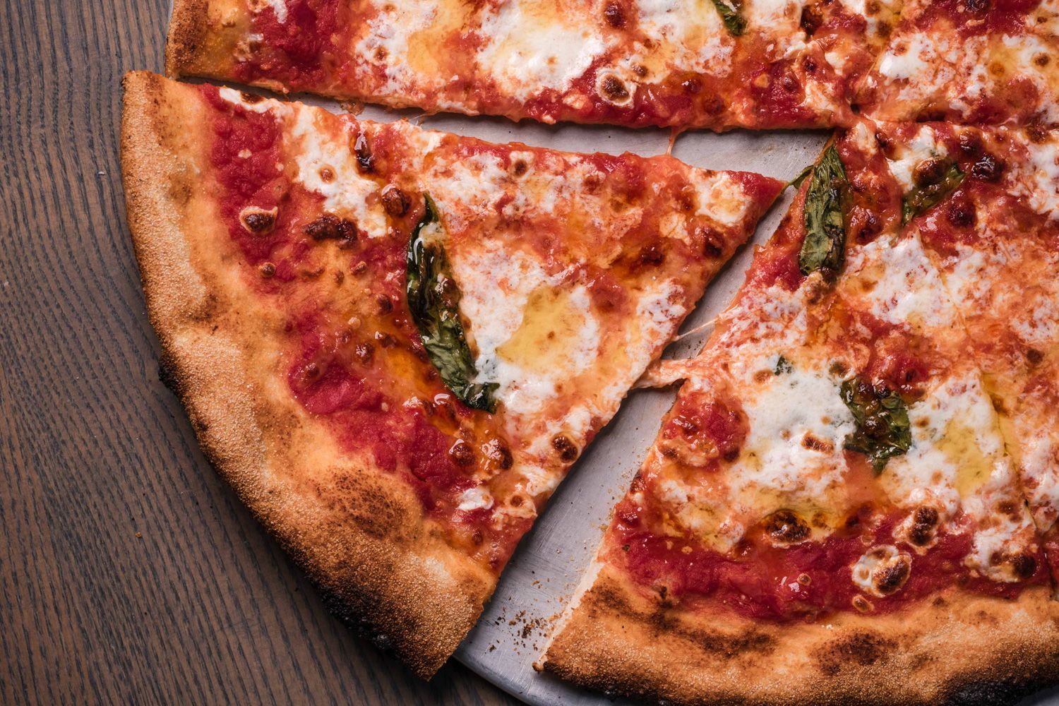 Close-up of a sliced coal-fired Margherita pizza on a silver tray, featuring melted mozzarella, fres