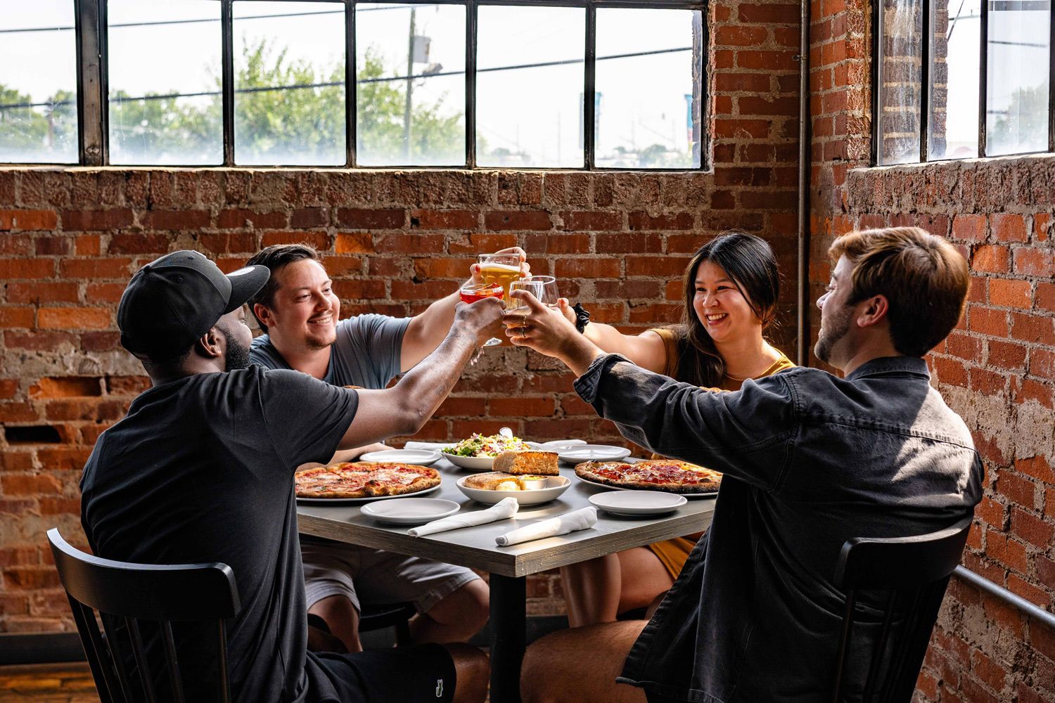 Group of friends toasting with drinks at Nicky’s Coal Fired in Nashville, enjoying coal-fired pizzas