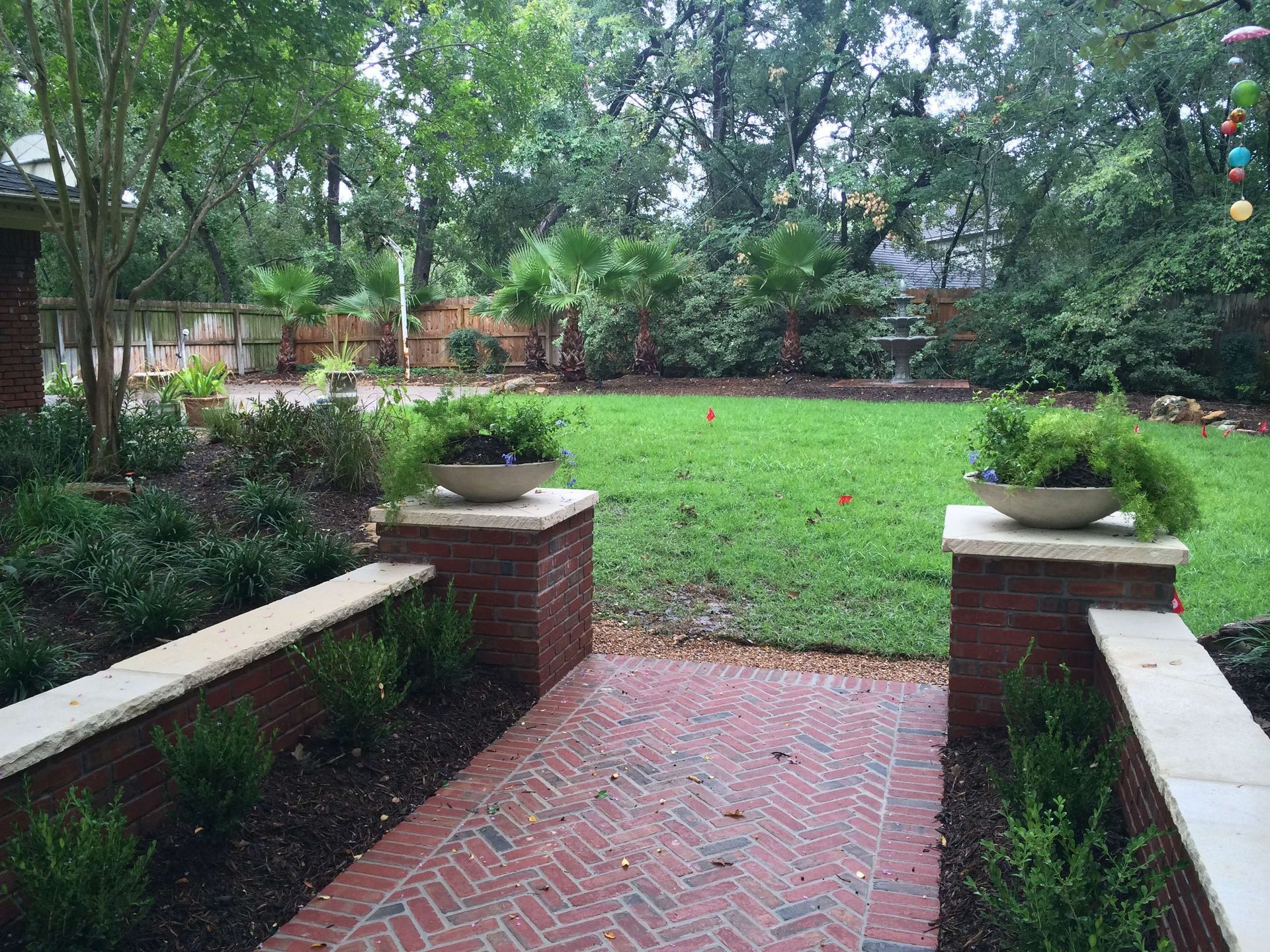 A brick walkway leading to a large lush green lawn.