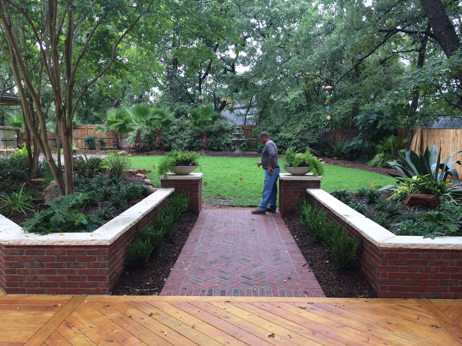 A man is standing on a brick walkway in a garden.