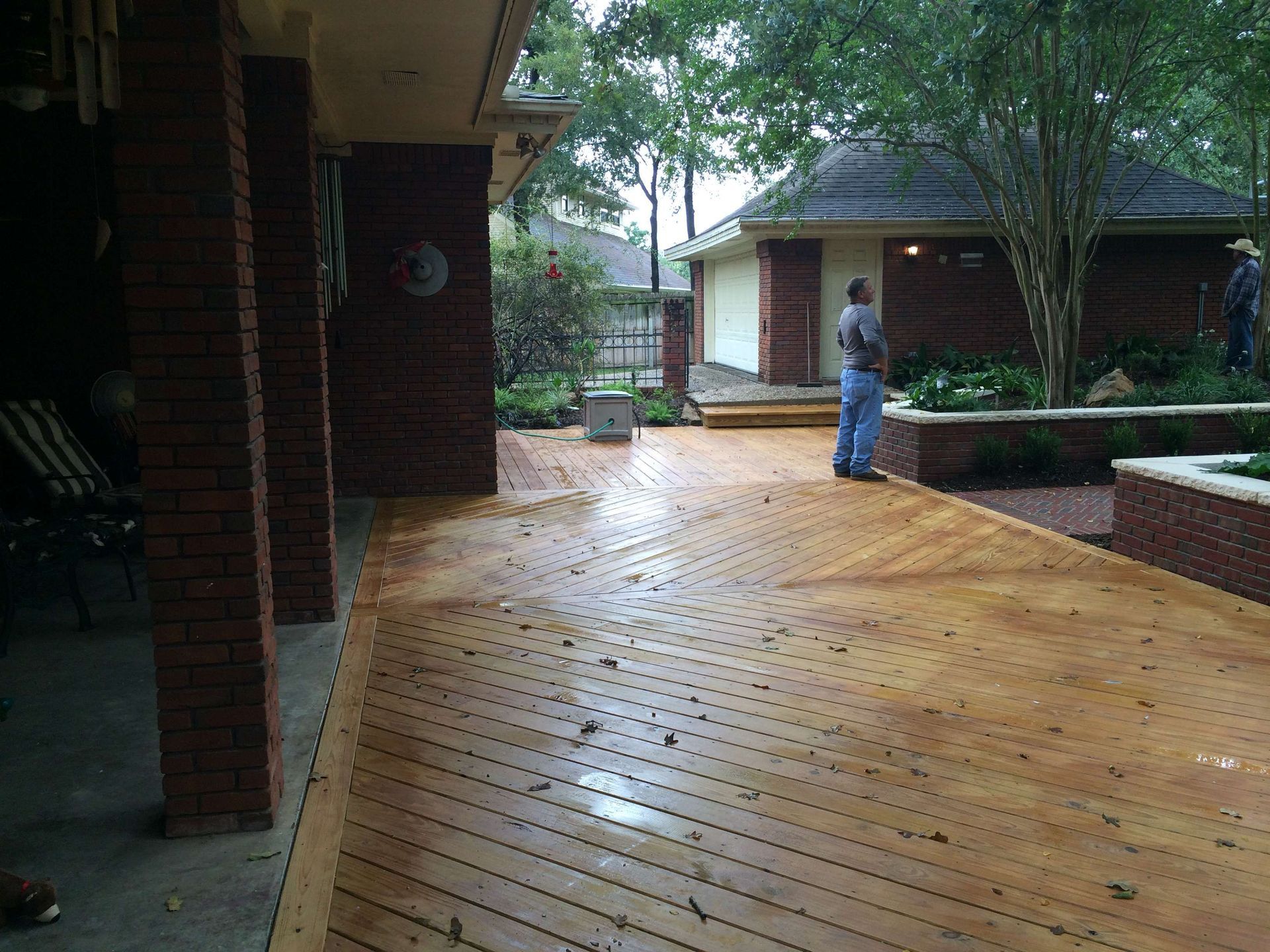 A man standing on a wooden deck in front of a brick house